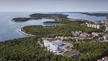 Vista aérea de un pueblo costero con un extenso complejo hotelero, rodeado de densos bosques y una bahía con varias islas.