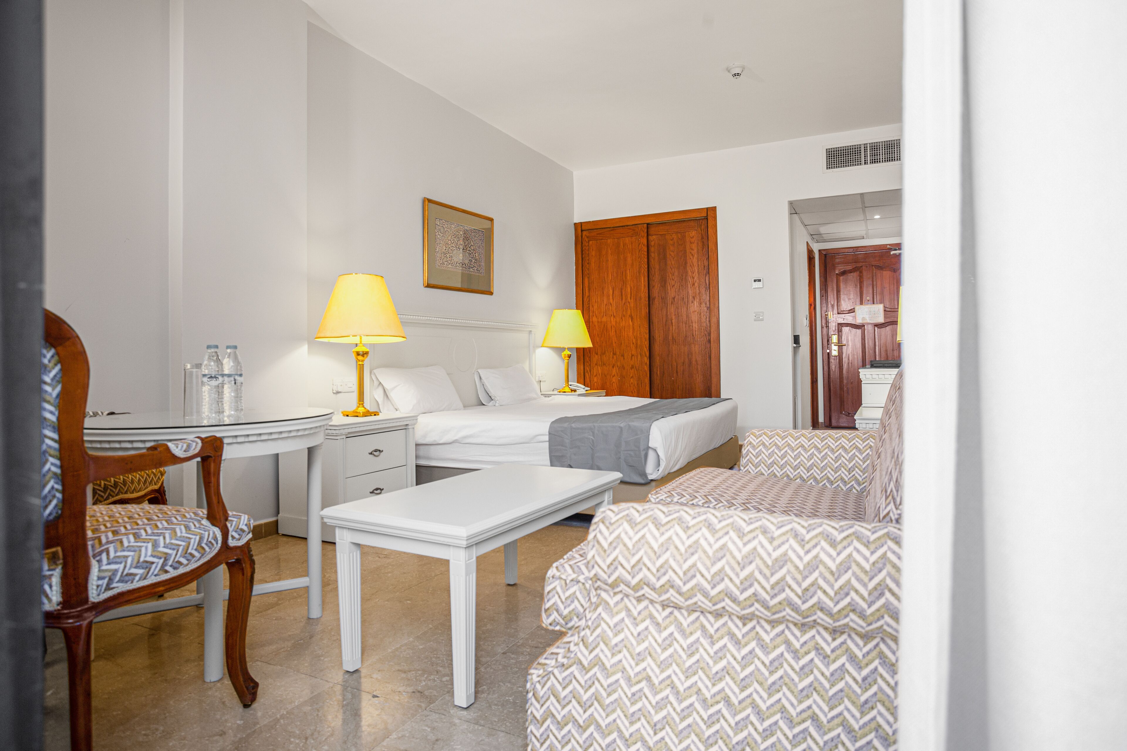 Quarto de hotel com uma cama, duas mesas de cabeceira, uma escrivaninha, uma cadeira e um sofá.