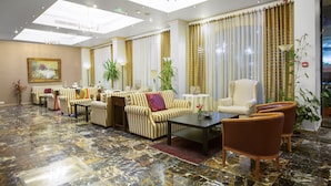 A spacious lobby with a marble floor, striped sofas, a coffee table, and a large armchair. - Grand Hotel Madaba (Madaba)