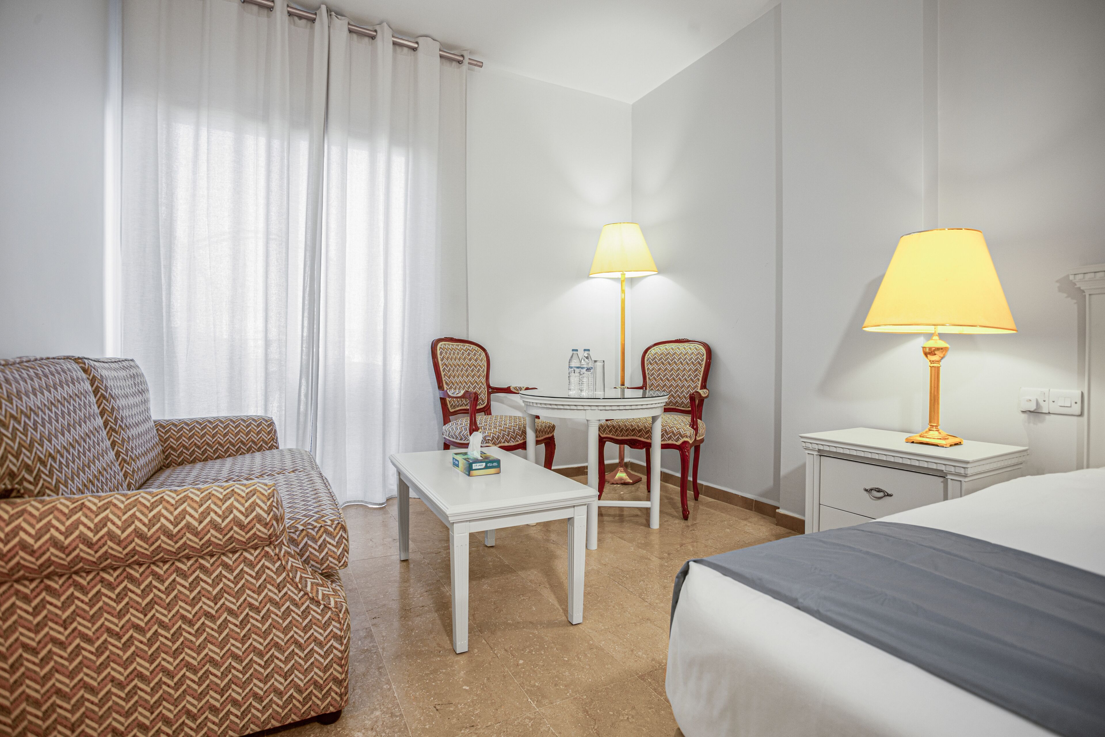 A hotel room with a bed, a sofa, a table, two chairs, a lamp, and a nightstand.