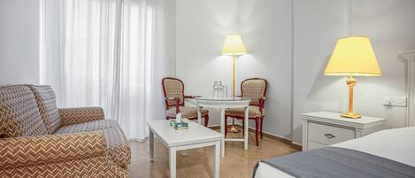 A hotel room with a bed, a sofa, a table, two chairs, a lamp, and a nightstand.
