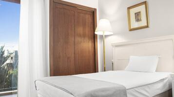 Ein Hotelzimmer mit Bett, Nachttisch, Lampe, Holztür und einem Fenster mit Vorhängen.