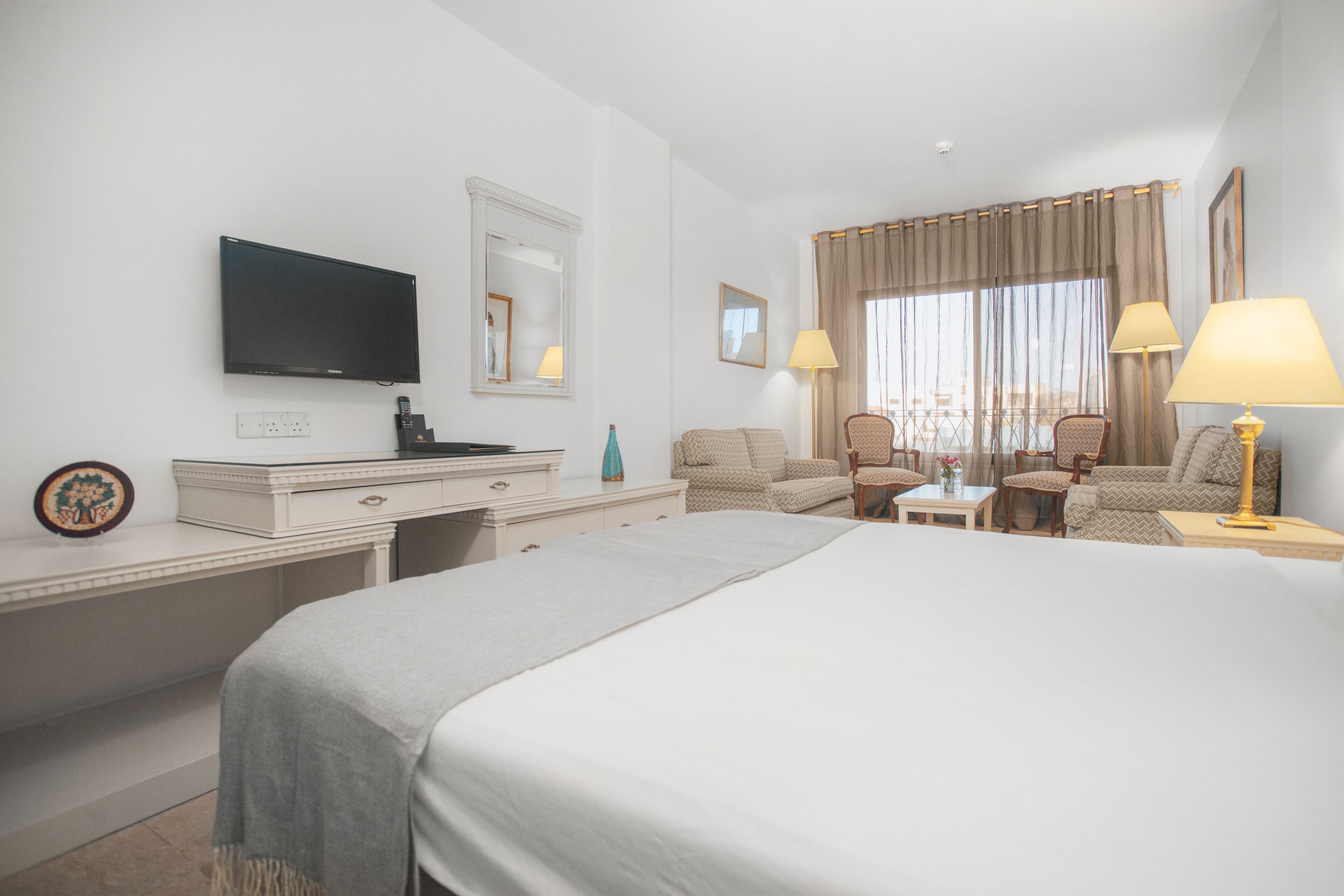 A hotel room with a bed, a desk, a chair, a TV, and a window with curtains.