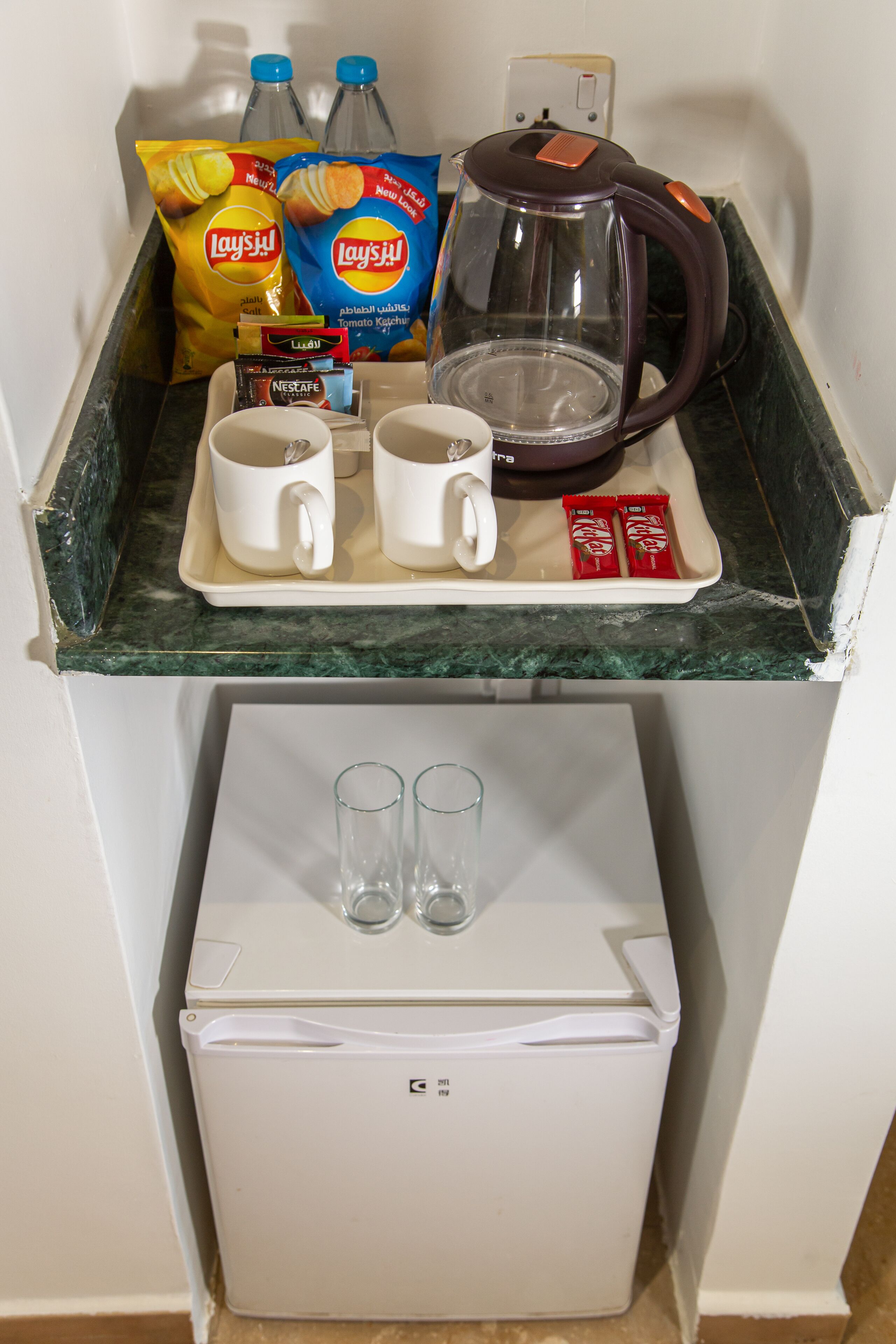 En köksbänk med en kaffebryggare, två vita muggar, ett bricka med två paket Nescafe och två påsar Lay’s-chips.