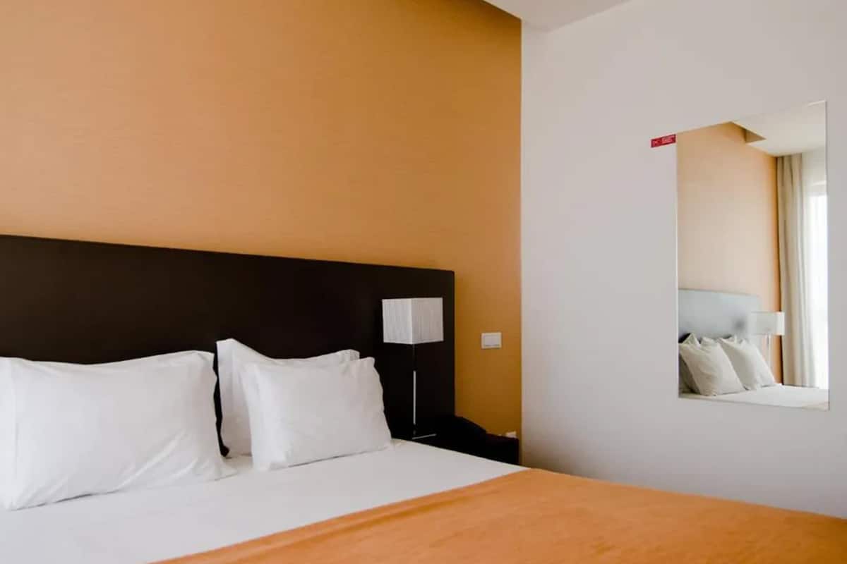 A hotel room with a bed, a nightstand, a lamp, and a wall-mounted mirror.