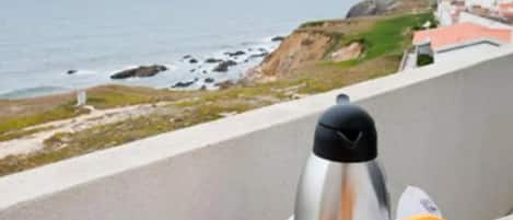 Ein Frühstückstisch auf einem Balkon mit Blick aufs Meer, mit Obstteller, Gläsern Saft, einer Kaffeekanne und einem Croissant.