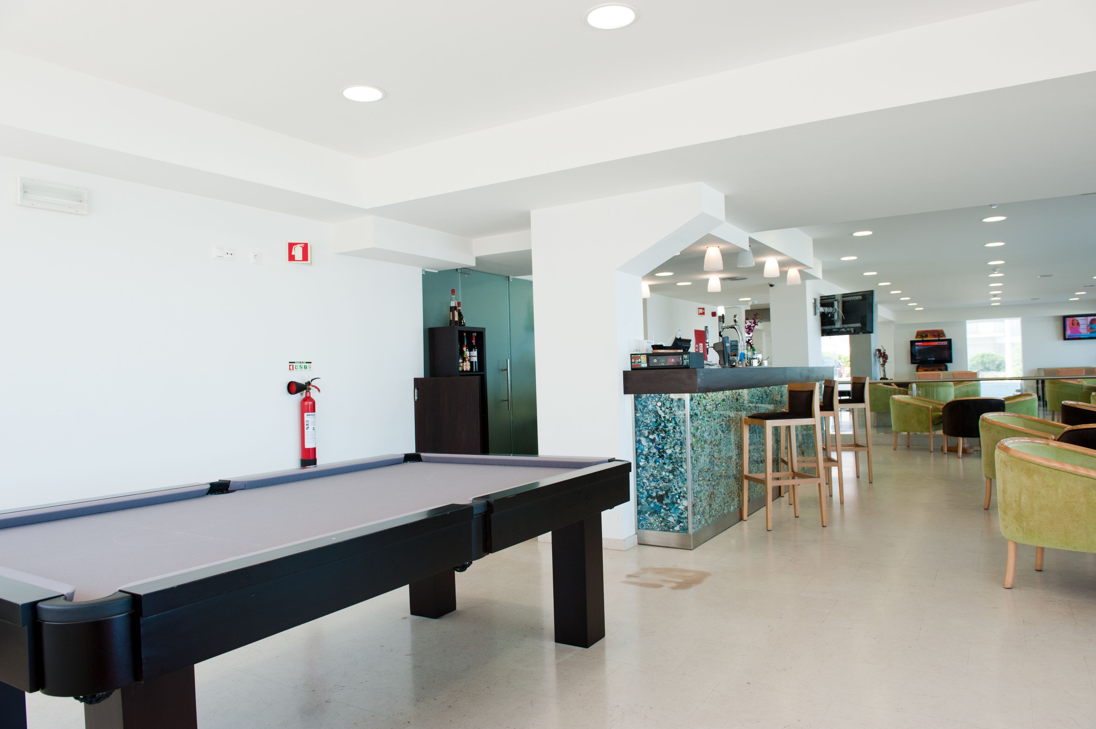 A pool table in a modern indoor space with a bar area, seating, and a television.
