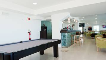 A pool table in a modern indoor space with a bar area, seating, and a television.