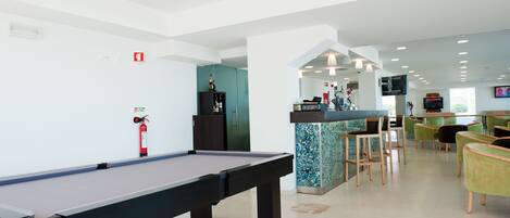 A pool table in a modern indoor space with a bar area, seating, and a television.