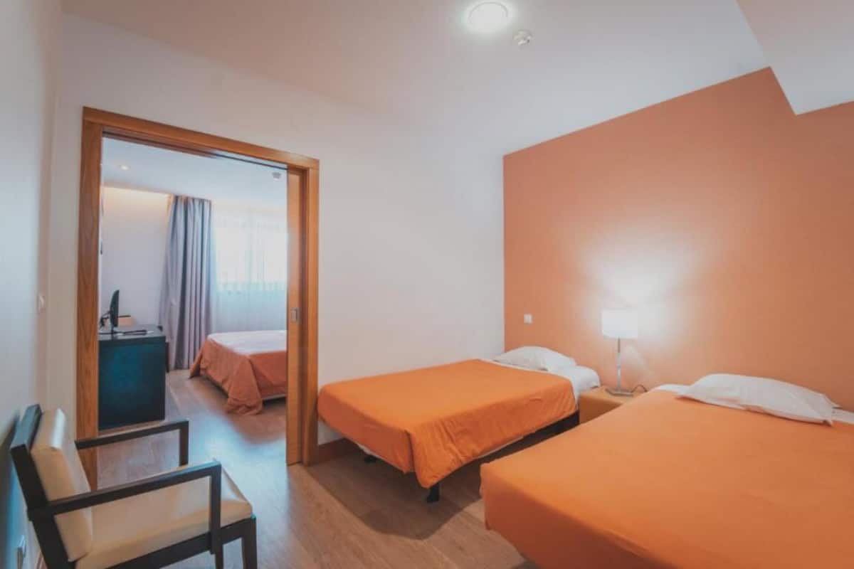 A hotel room with two beds, a desk, and a chair.