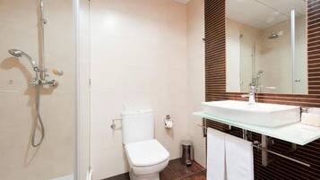 Um banheiro moderno com box de vidro, vaso sanitário branco e pia de vidro com painel de madeira no fundo.