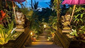 Un chemin de pierre bordé de statues et d’une végétation tropicale luxuriante mène à l’entrée d’un temple.