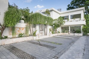 A modern building with a courtyard, featuring a large tree, potted plants, and a decorative wall. - Awila Villa Kuta (Kuta)