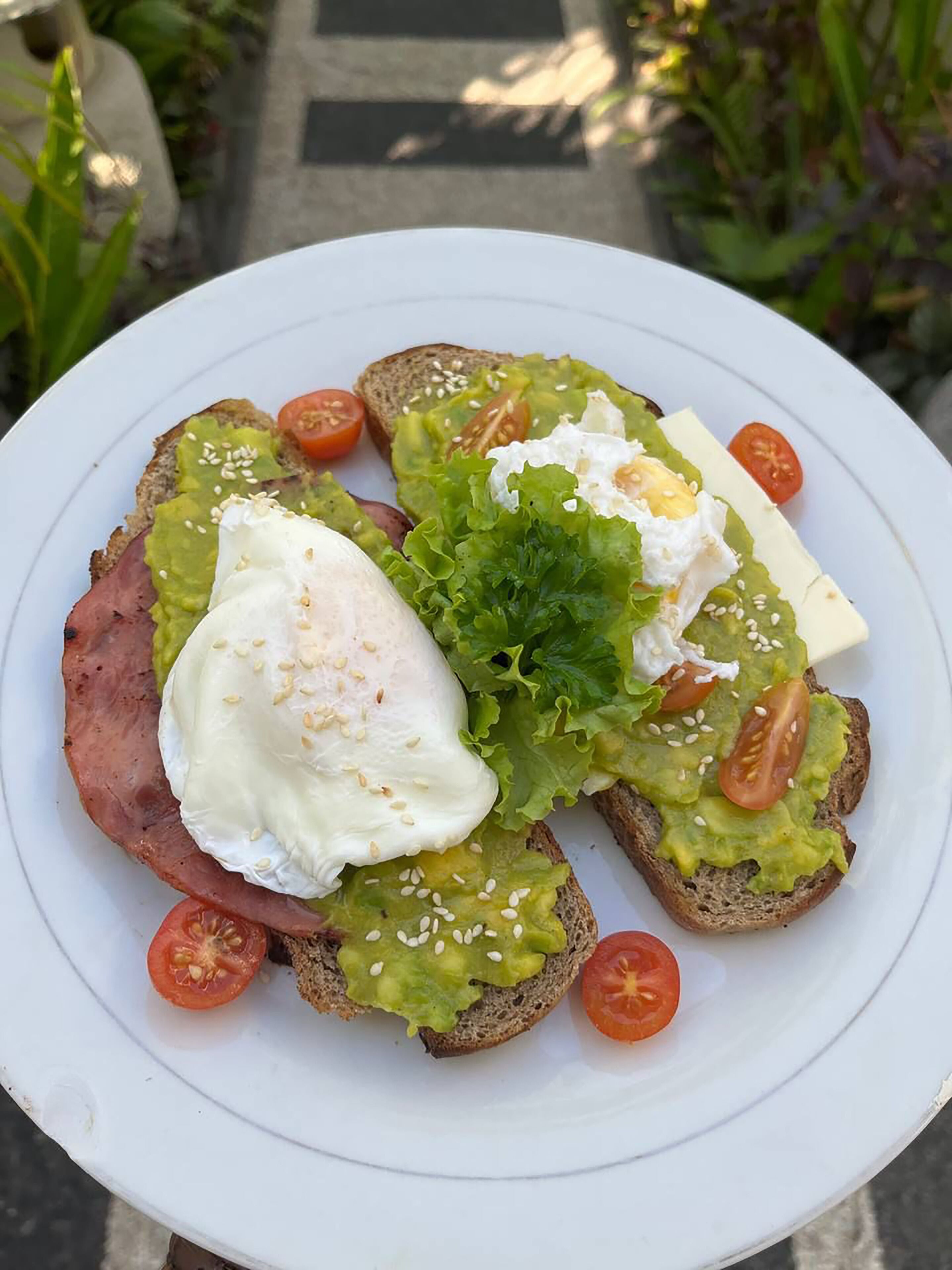 Un plato con tostada cubierta de aguacate, un huevo pochado, lechuga y rodajas de tomate.