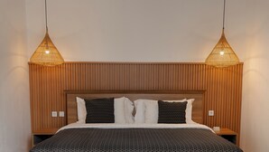 Une chambre moderne avec une tête de lit en bois, une couvre-lit à motifs et deux lampes suspendues.