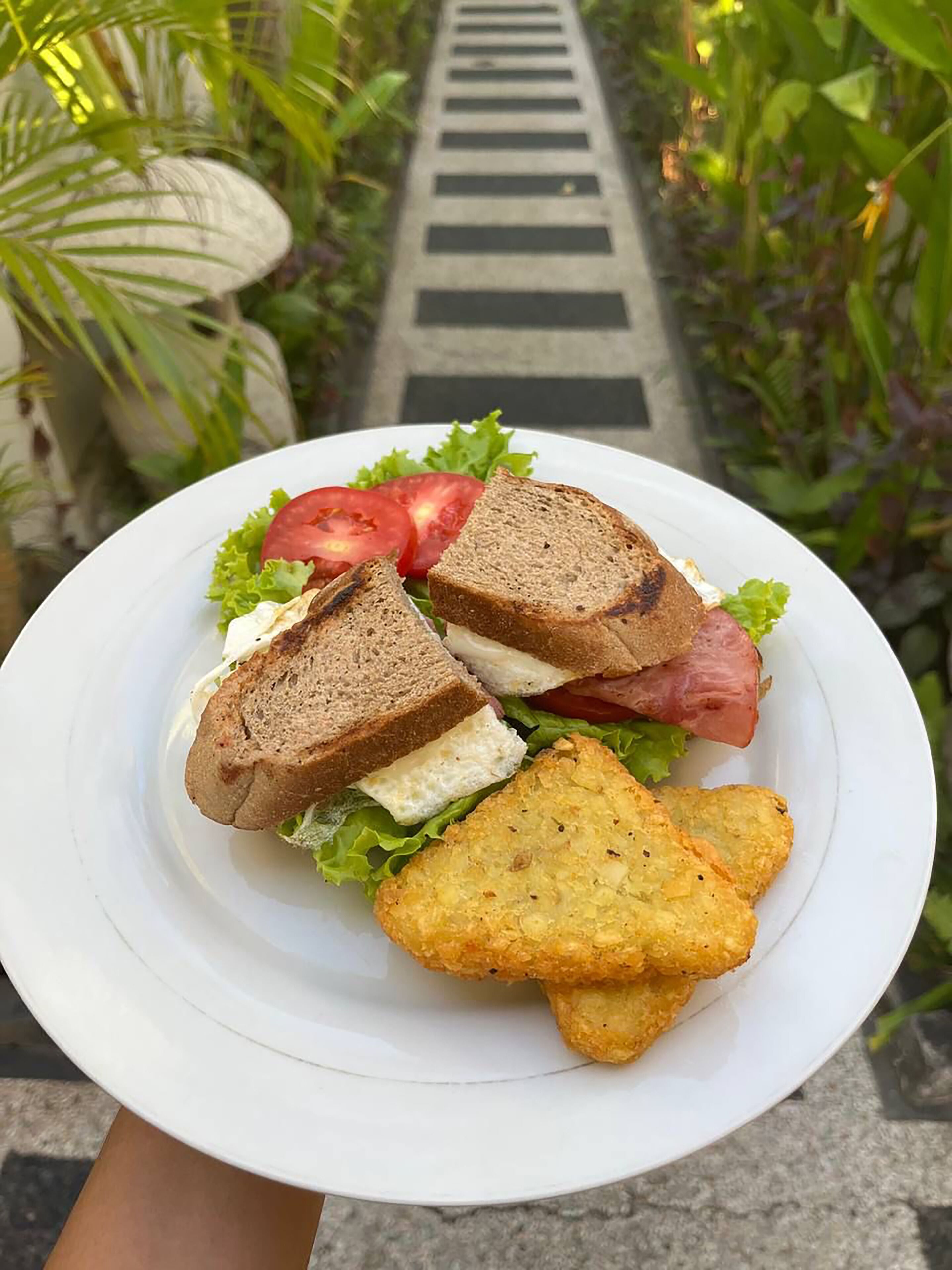 A plate with a sandwich, tomato slices, lettuce, and fried potato chips.