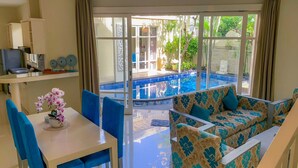 A room with a dining table, chairs, a sofa, and a view of an outdoor swimming pool. - Awila Villa Kuta (Kuta)