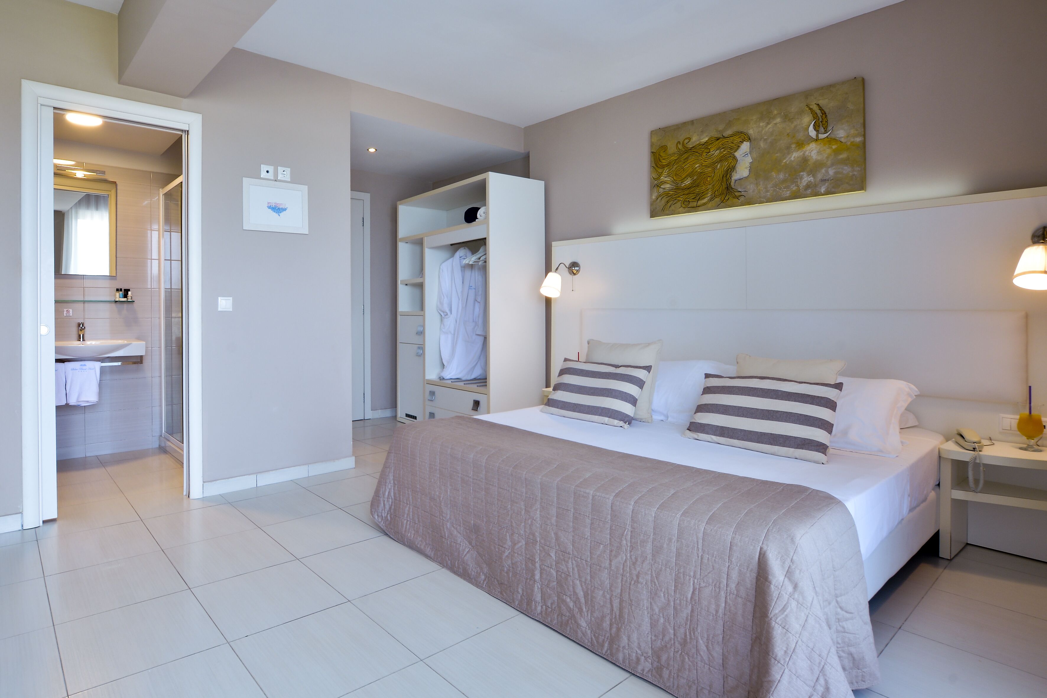 Un dormitorio con una cama grande, una mesita de noche con lámpara, un armario y un baño visible a través de una puerta abierta.