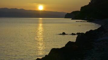 A sunset over a calm sea with rocky shores and distant mountains.