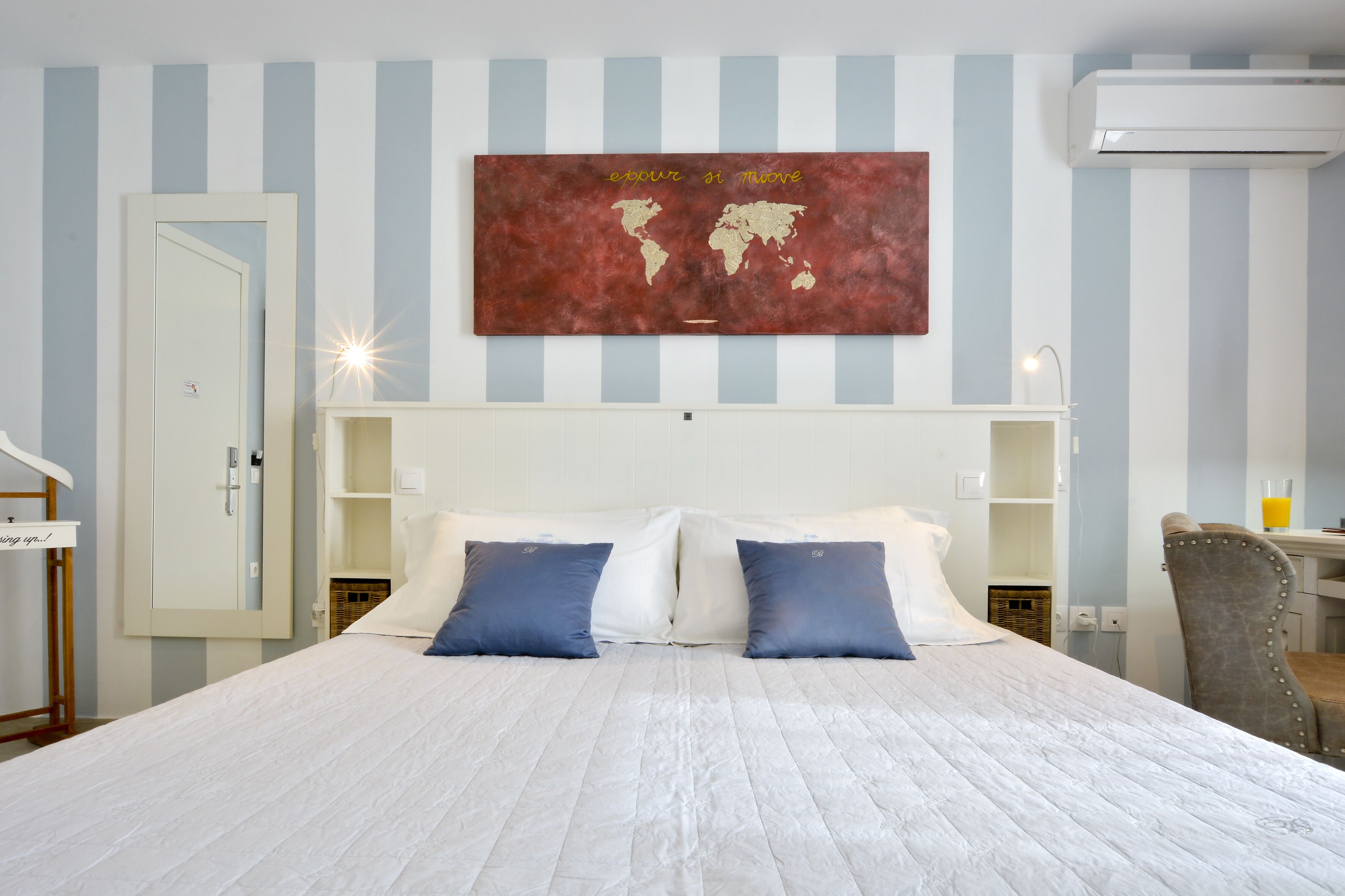 A neatly arranged hotel room with a large bed, a world map artwork on the wall, and a small desk with a chair.
