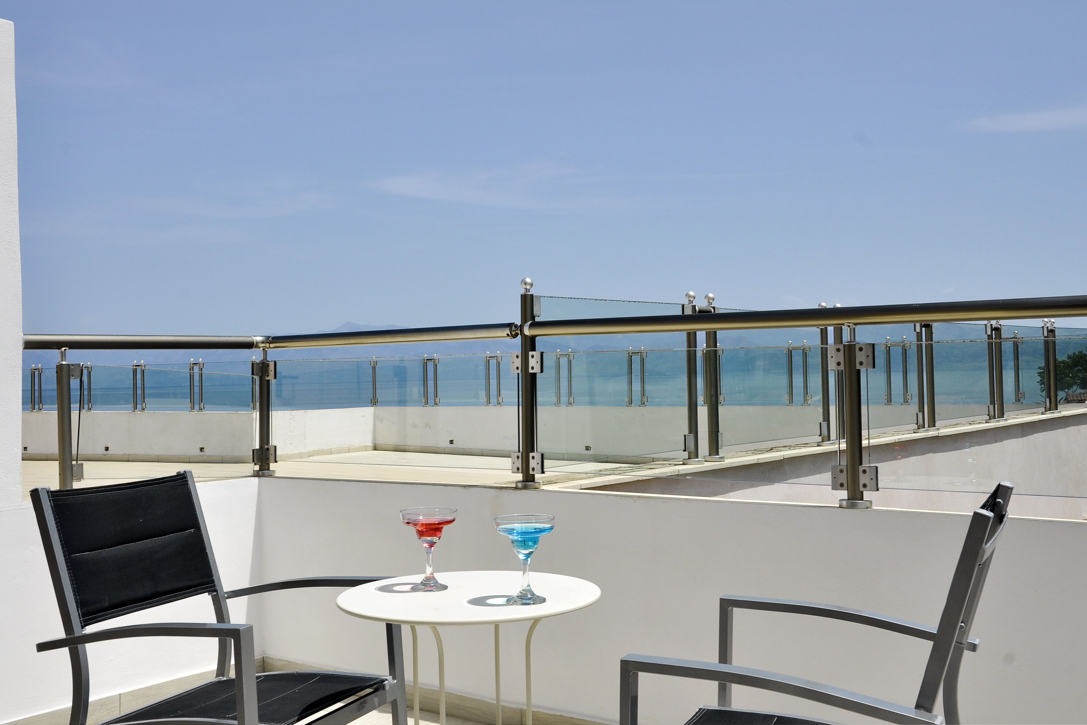 En balkon med to stole, et lille bord, gelænder og havudsigt.