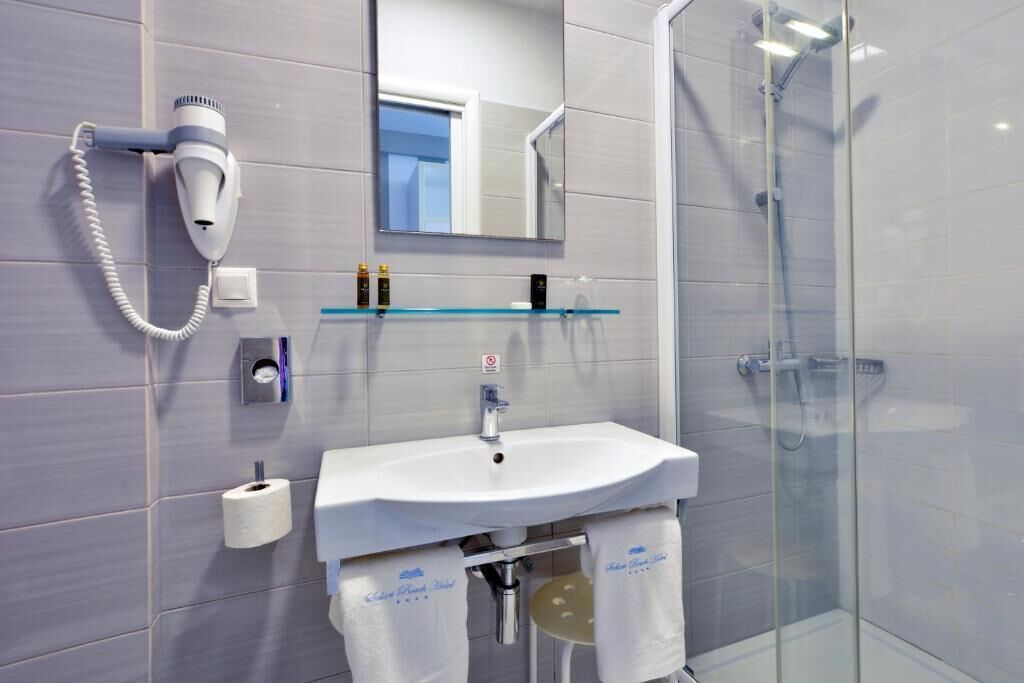 A modern bathroom with a white sink, a hairdryer, a glass shower enclosure, and a mirror above the sink.