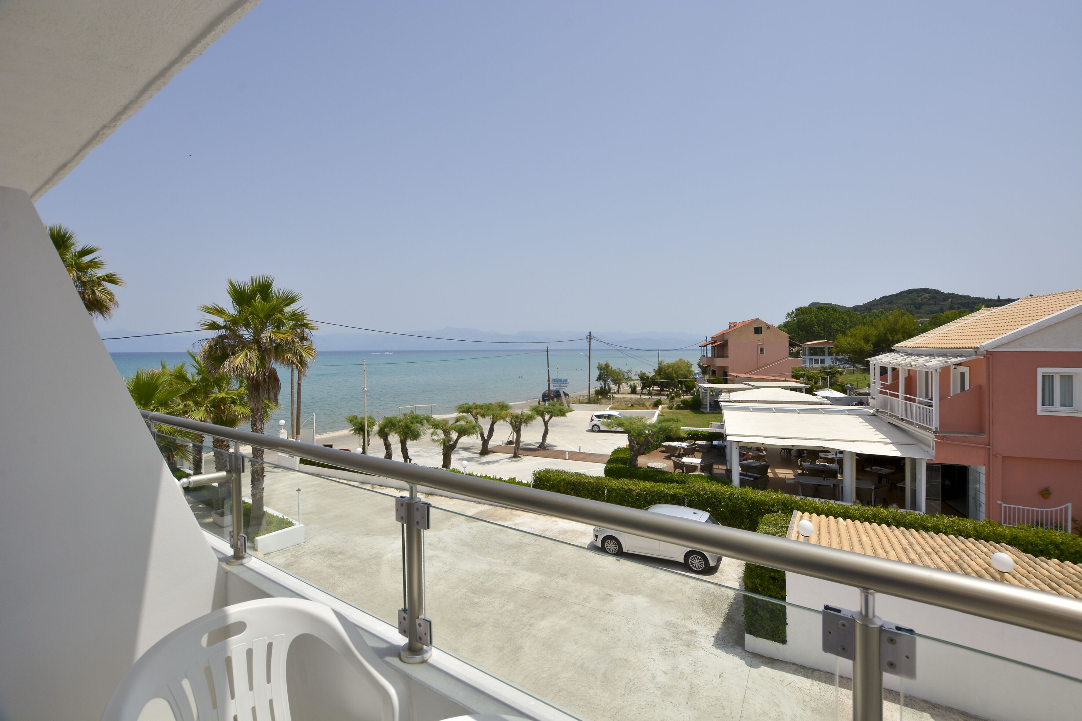 A balcony with a view of a beach, palm trees, and a building with a tiled roof.