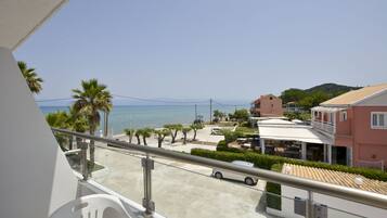 A balcony with a view of a beach, palm trees, and a building with a tiled roof.