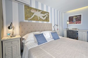 Un dormitorio ordenado con una cama grande, dos mesitas de noche, una mesita auxiliar y un aparador.