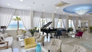 A spacious living room with a grand piano, plush armchairs, and a view of the ocean. - Sidari Beach Hotel (Corfu)