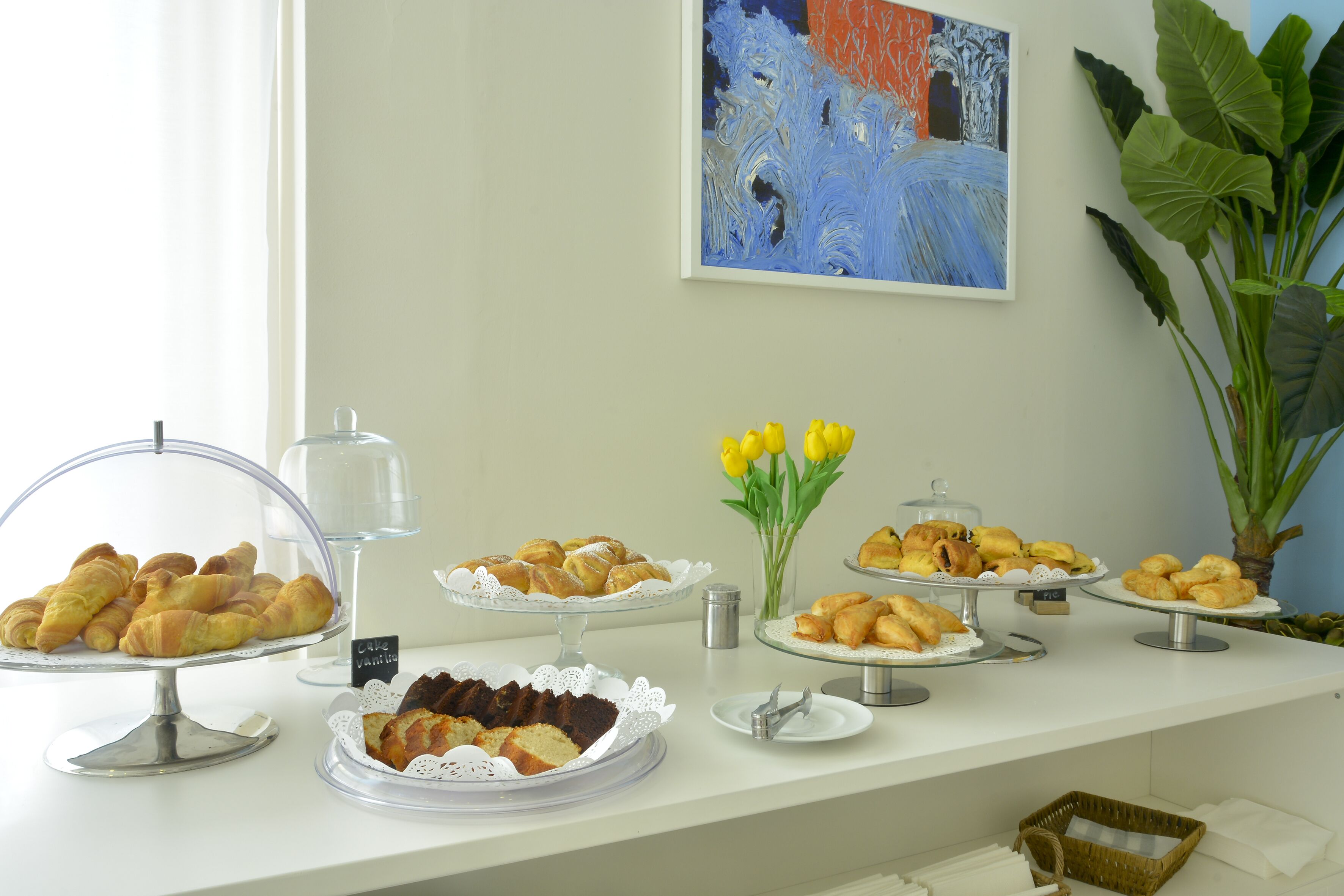 A buffet table with various pastries and a vase of yellow tulips.