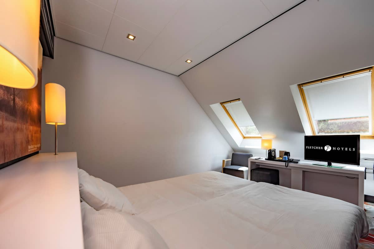 Een moderne hotelkamer met een groot bed, een bureau met een televisie en een dakraam.