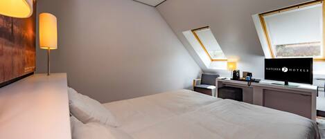 Una habitación de hotel moderna con una cama grande, un escritorio con televisor y un tragaluz.