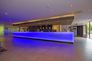 Mostrador de recepción de hotel con una barra iluminada en azul, una cámara de seguridad y una puerta visible a la derecha.
