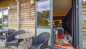 Een terras met rieten stoelen en een kleine ronde tafel, een schuifdeur naar een keuken, en een vloerkleed met een patroon.