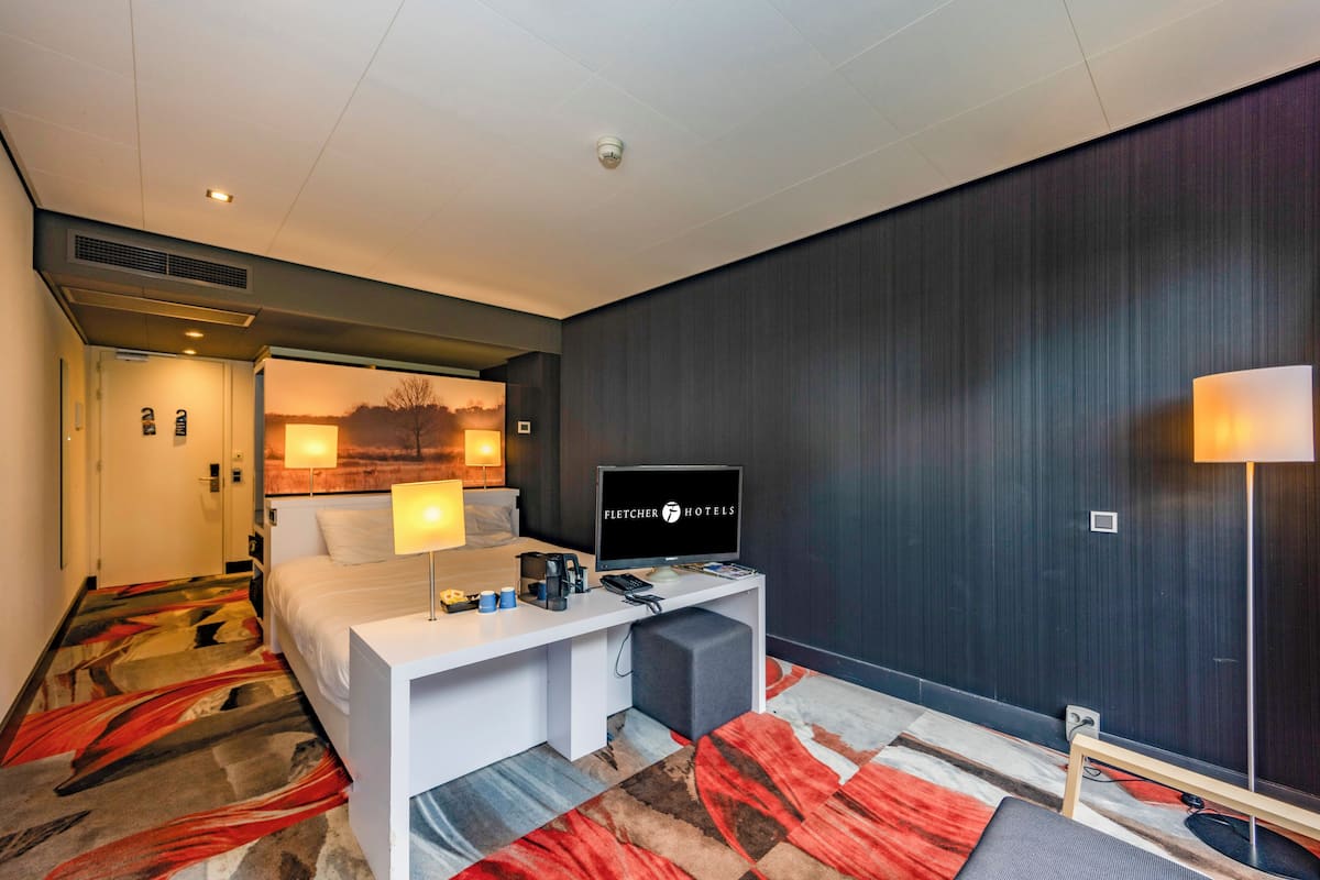 Een hotelkamer met een bed, bureau, televisie en uitzicht op de omgeving.