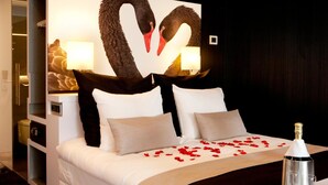 Een moderne hotelkamer met een groot bed, een decoratieve wand met zwanen, een minibar en een fles champagne.