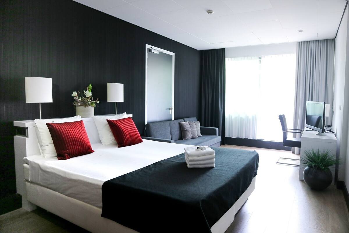 Een moderne hotelkamer met een groot bed, een bureau met een computer, een bank en een televisie.