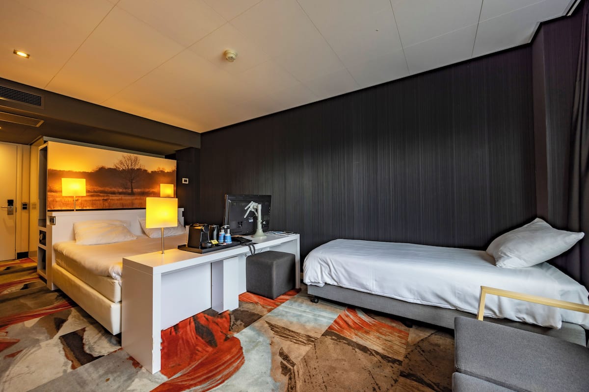 Een hotelkamer met een bed, een bureau, een stoel en uitzicht op een zonsondergang.
