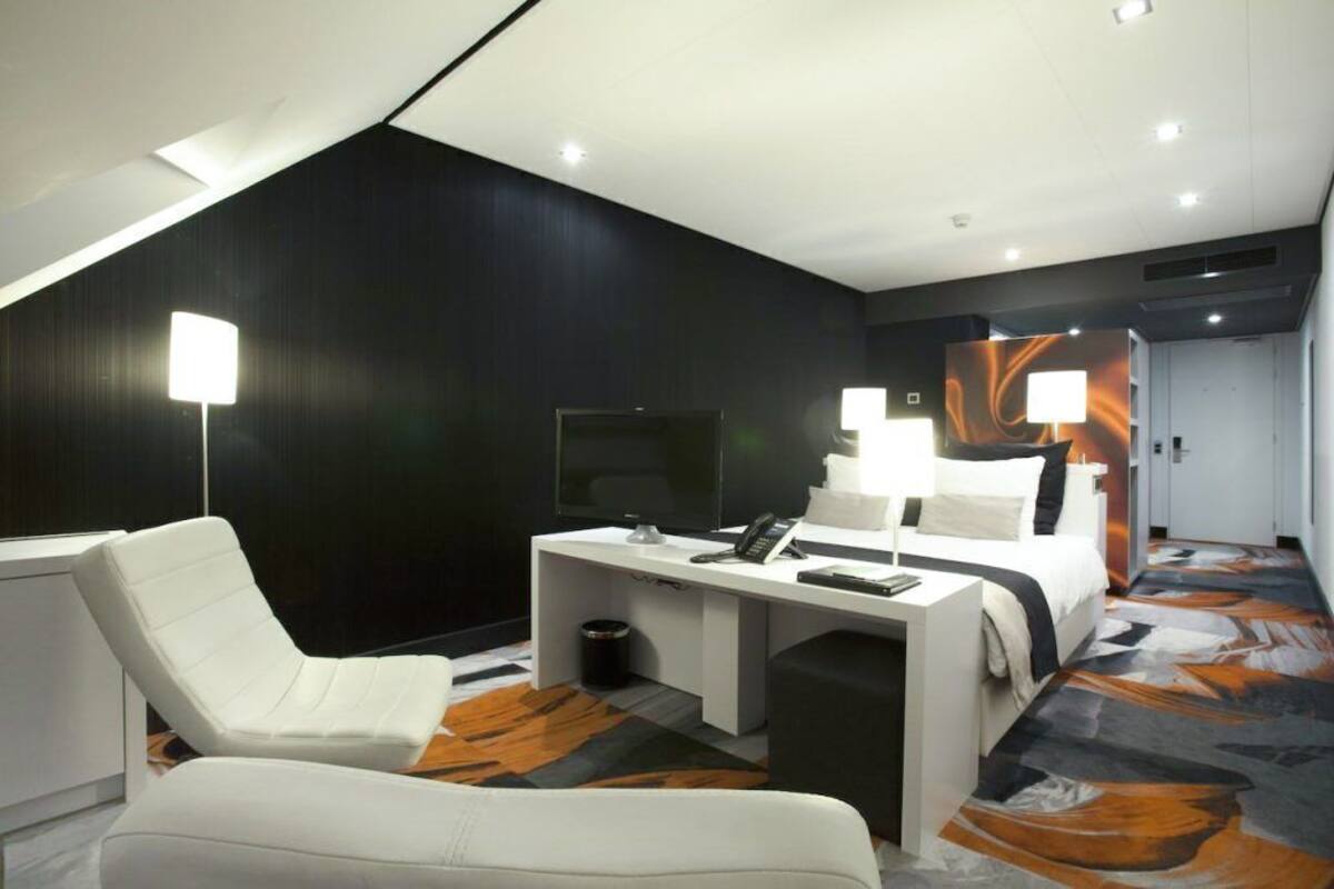 Een moderne hotelkamer met een bed, bureau, stoel en een groot raam.