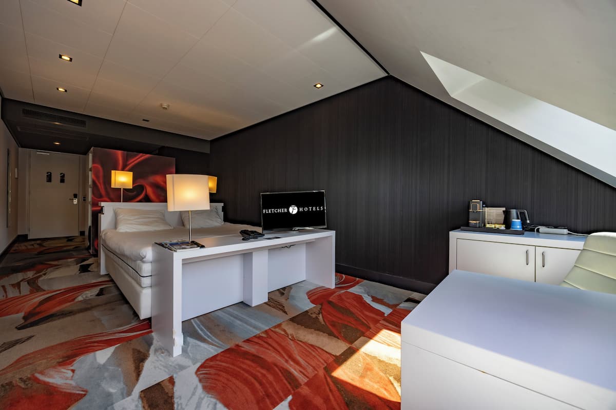 Een moderne hotelkamer met een bed, een bureau, een televisie en een minibar.