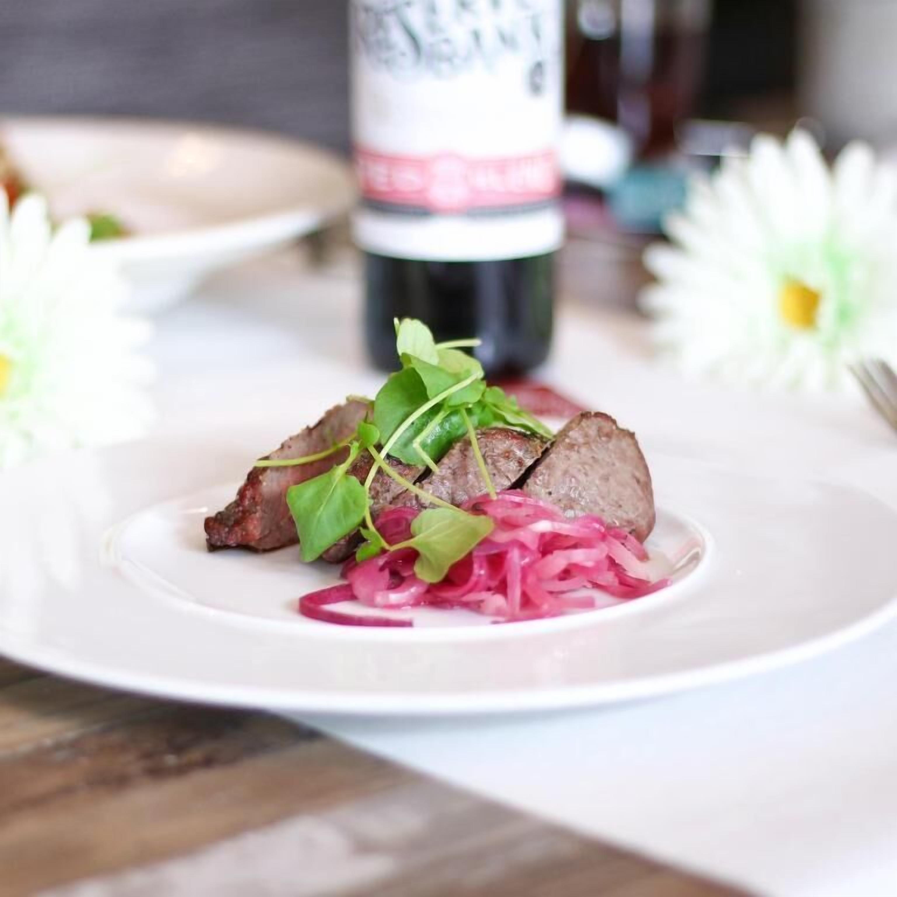 A plate with sliced meat, greens, and pickled vegetables.
