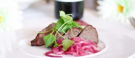 A plate with sliced meat, greens, and pickled vegetables.