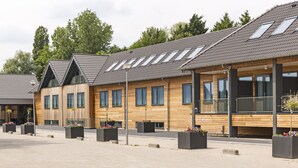 Een modern gebouw met een schuin dak, grote ramen en buitenplanters met bloemen.