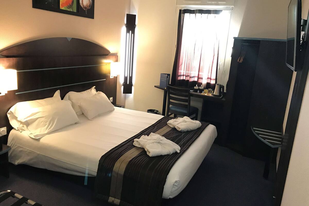 A hotel room with a bed, a desk, a chair, a wardrobe, and a window with curtains.