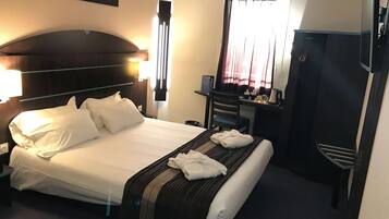 Habitación de hotel con cama, escritorio, silla, armario y ventana con cortinas.