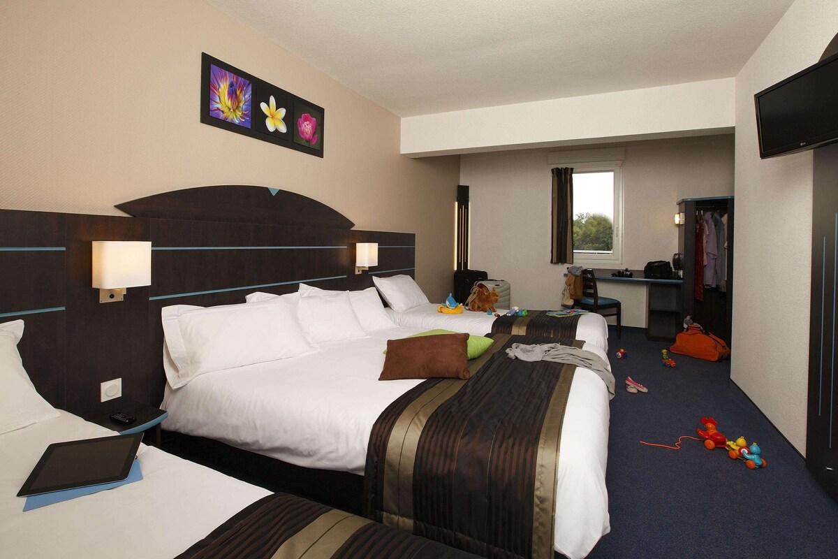 A hotel room with a large bed, bedside tables, a desk, and a television.