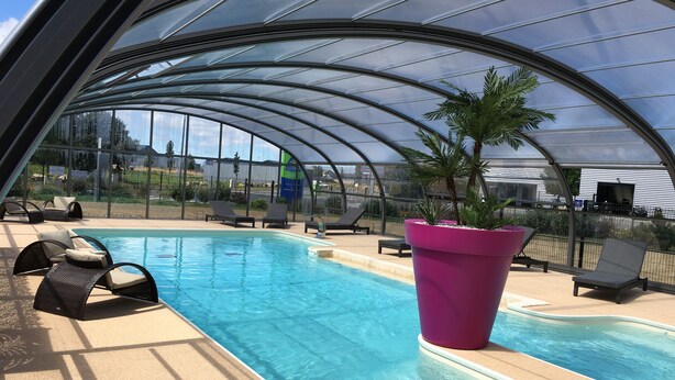 A covered swimming pool with lounge chairs and a large planter.