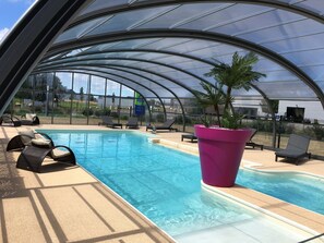 A covered swimming pool with lounge chairs and a large planter.
