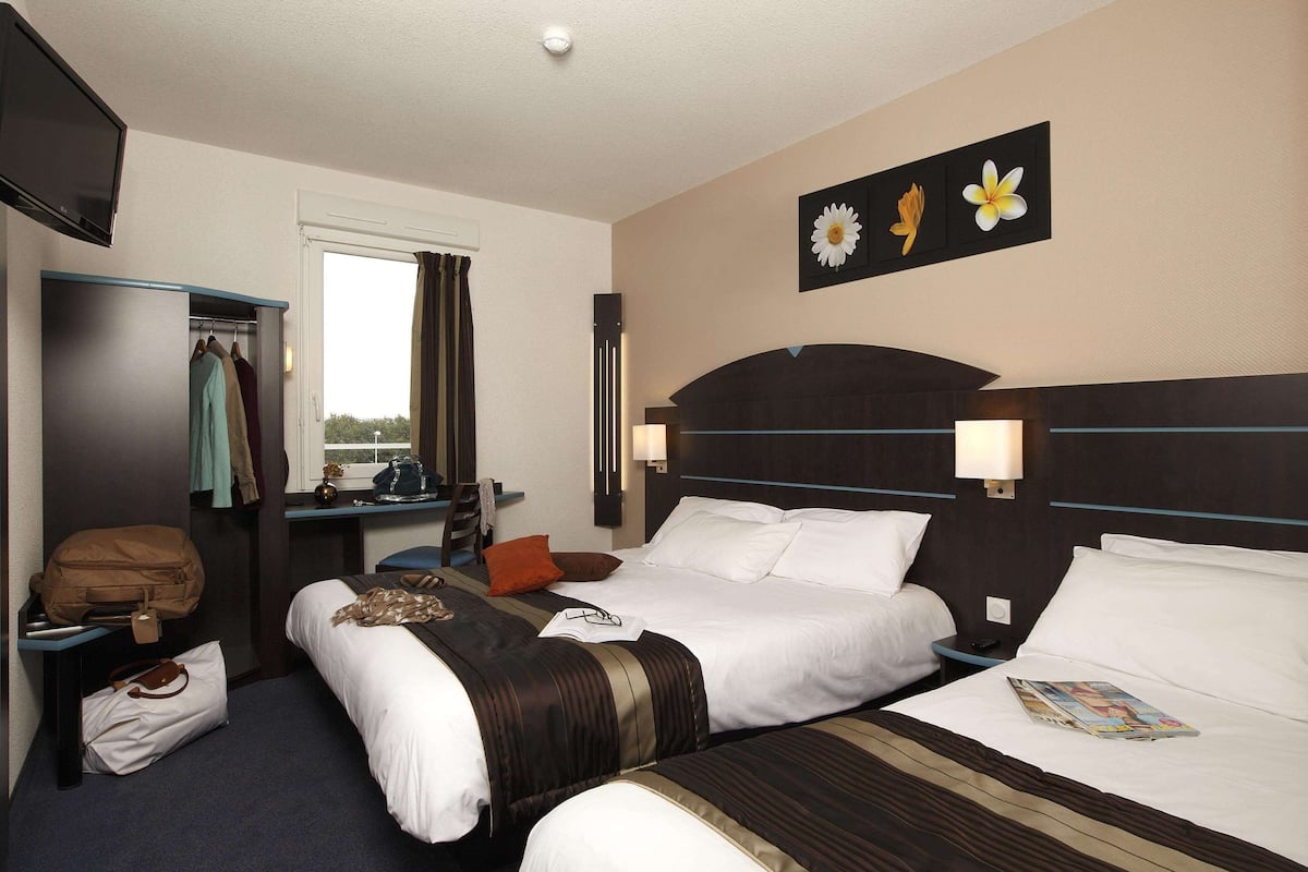 A hotel room with two beds, a desk, a wardrobe, and a window.